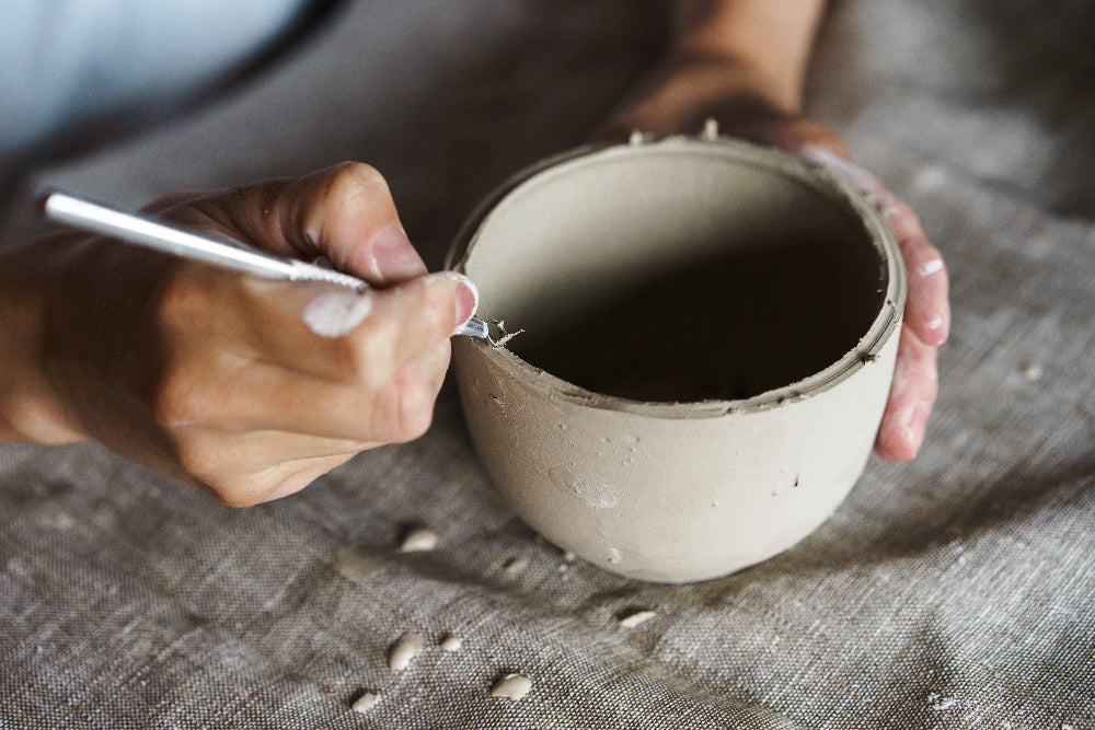 close up of hands trimming pottery bowl with tool
